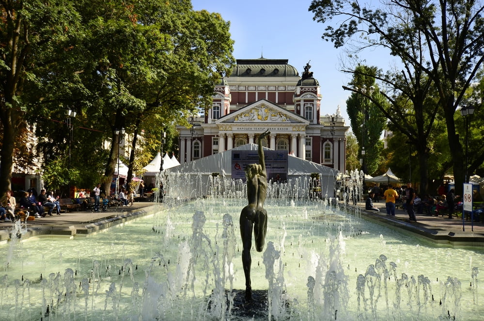Sofia, Bulgaria: People relaxing around the pool with small fountains and female sculpture in front of the National Theater Iwan Vazov